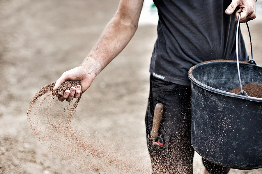 A person is holding a bucket from which they are sowing