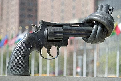 A bronze sculpture "non-violence" of a revolver with its barrel tied in a knot, displayed outdoors in front of a row of international flags, the United Nations headquarters in New York. 