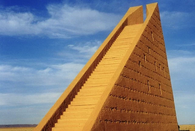 Large stone pyramid structure in a desert landscape under a blue sky