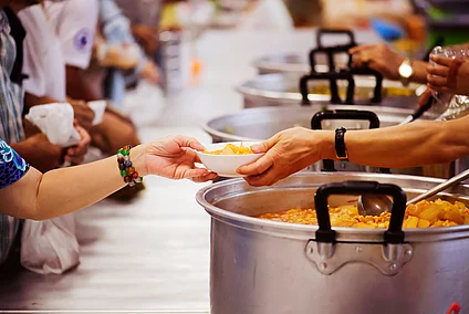 Volunteers serving hot food from large pots at a community meal or soup kitchen
