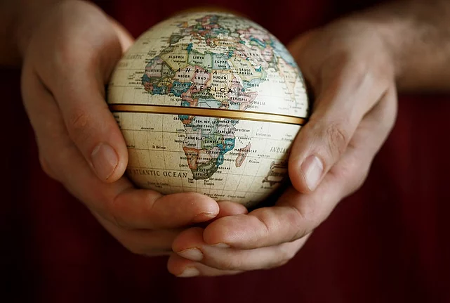 A pair of hands holding a small globe displaying the continent of Africa