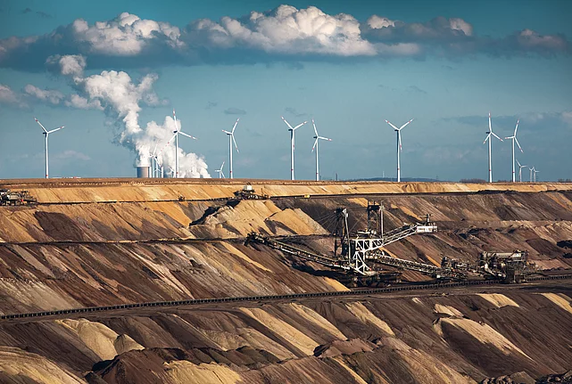Open-cast coal mine with excavators, wind turbines, and a power station in the background