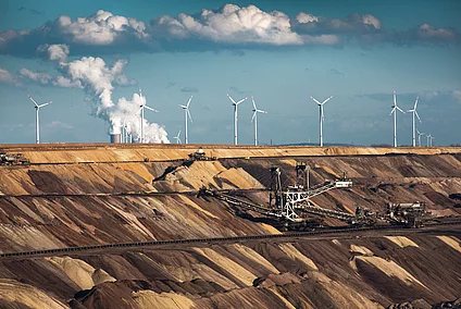Open-cast coal mine with excavators, wind turbines, and a power station in the background