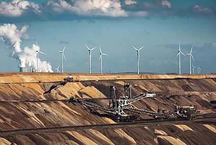 Open-cast coal mine with excavators, wind turbines, and a power station in the background