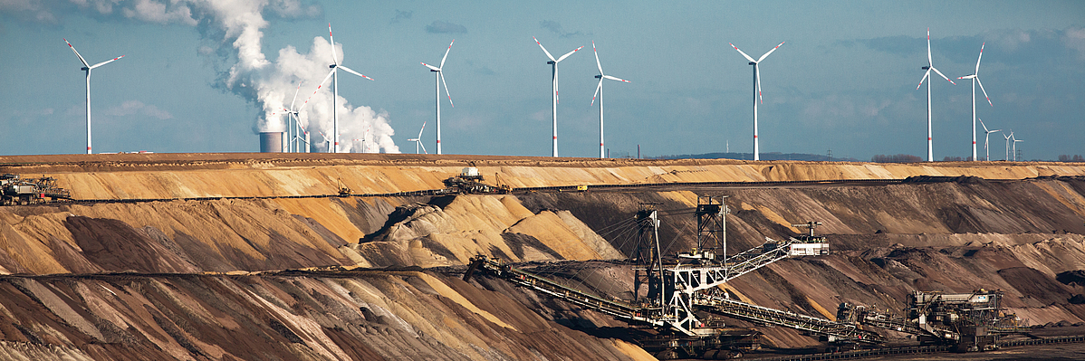 Open-cast coal mine with excavators, wind turbines, and a power station in the background