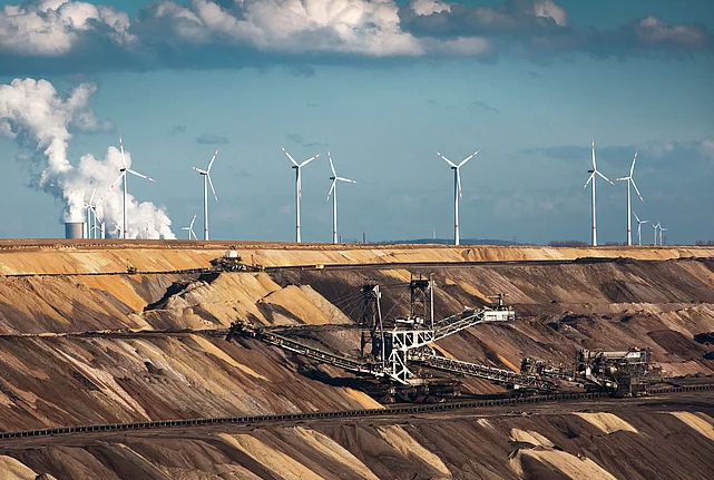 Open-cast coal mine with excavators, wind turbines, and a power station in the background