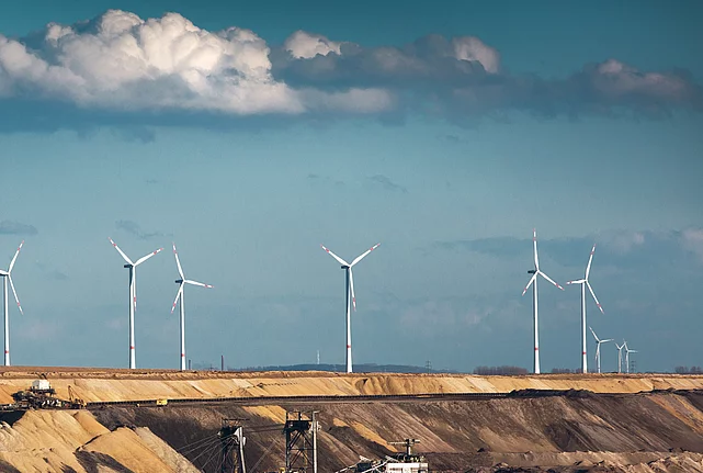 Open-cast coal mine with excavators, wind turbines, and a power station in the background