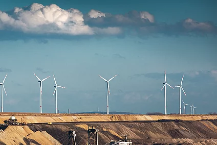 Open-cast coal mine with excavators, wind turbines, and a power station in the background