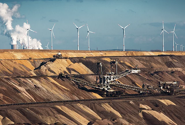 Open-cast coal mine with excavators, wind turbines, and a power station in the background