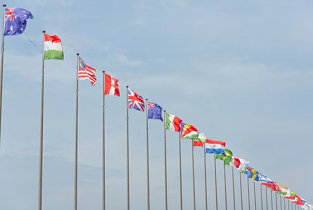 A row of international flags on flagpoles symbolizing multilateralism and diplomacy.