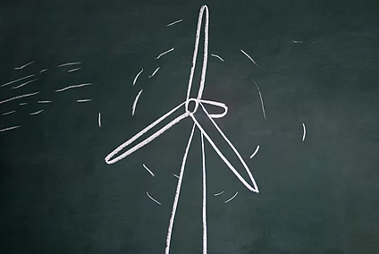 Person blowing on a chalk drawing of a wind turbine on a blackboard